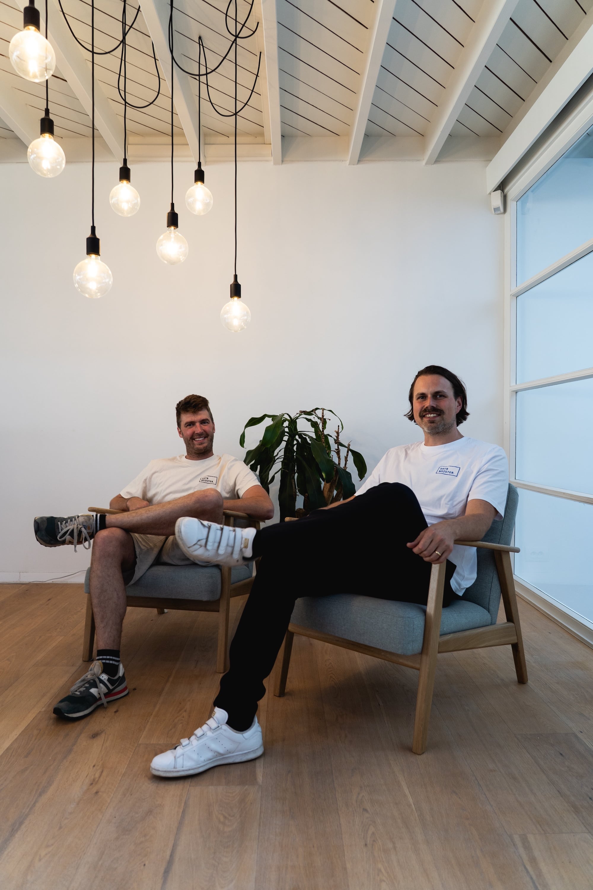 Two Datameister founders seated under a cluster of pendant lights in the Ghent studio